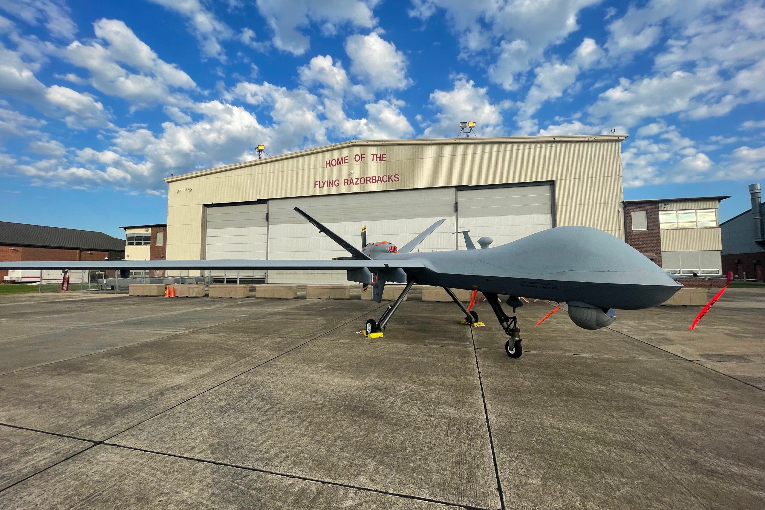 An MQ-9 Reaper drone parked on a USAF flightline in front of a hangar.